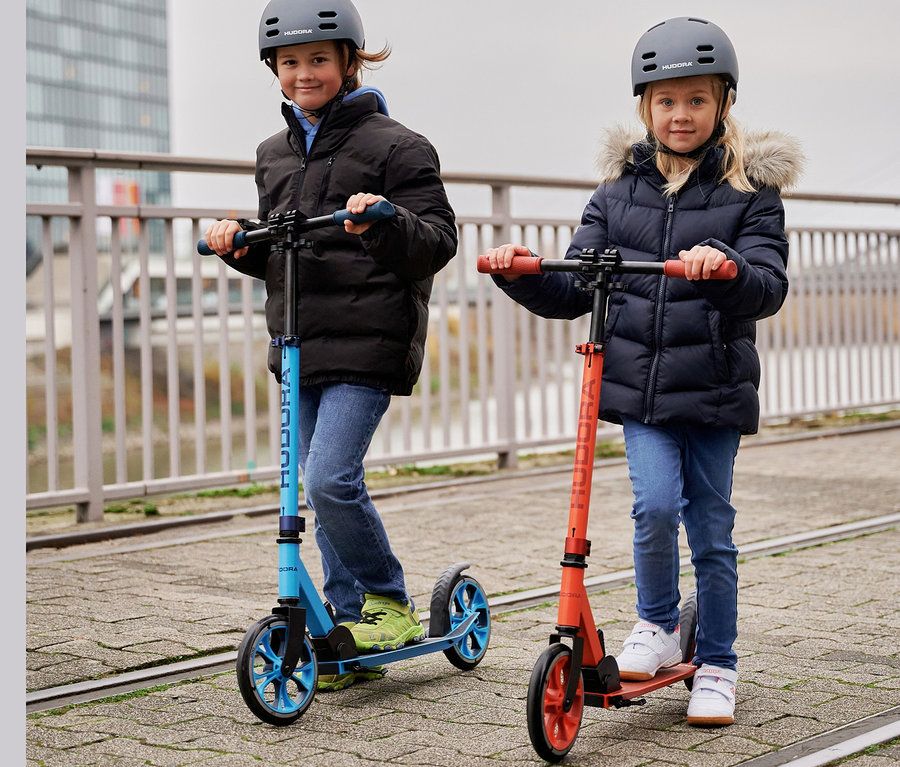 Zwei Kinder fahren auf einem blauen und einem roten HUDORA Scooter »Up 200«.