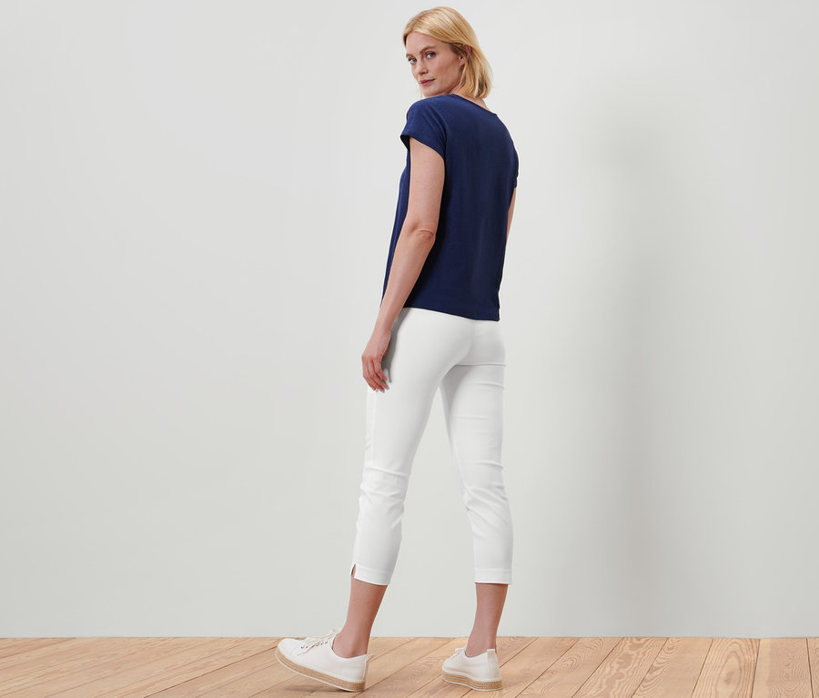 Eine Frau steht mit dem Rücken zur Kamera und trägt eine weiße 7/8-Stretchhose und ein dunkelblaues T-Shirt.