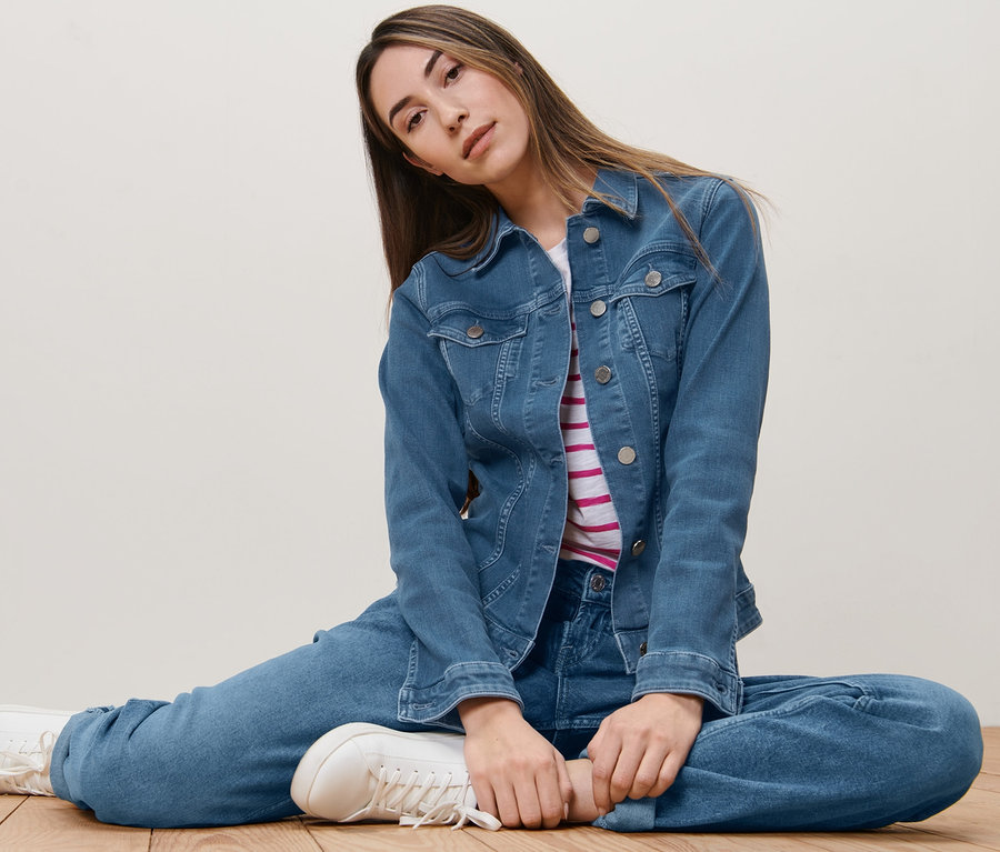 Frau sitzt auf dem Boden und trägt eine Jeansjacke.