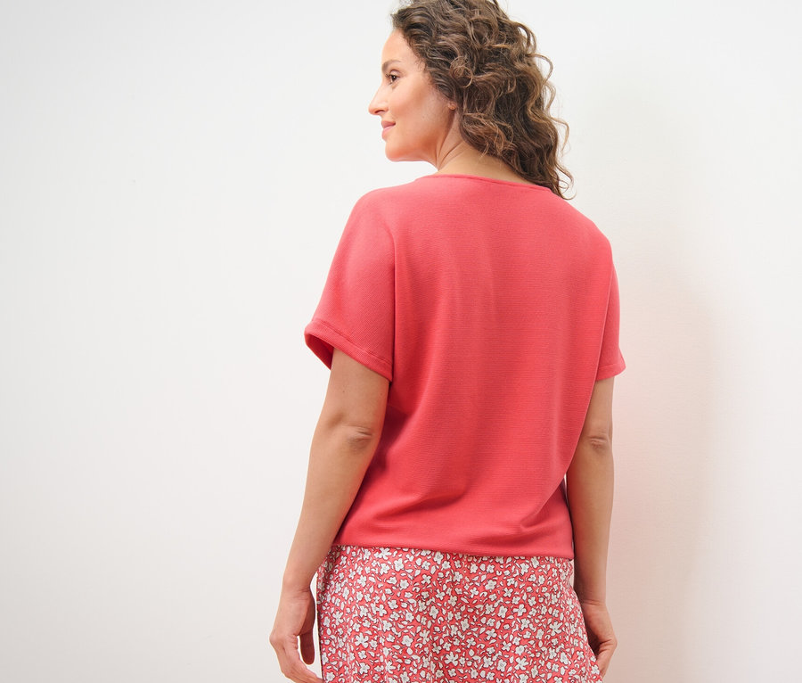 Frau blickt über die Schulter und trägt ein korallfarbenes Blusenshirt.