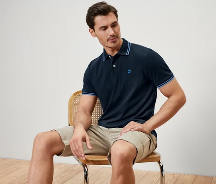 Mann sitzt auf einem Stuhl und trägt ein dunkelblaues Piqué-Poloshirt.