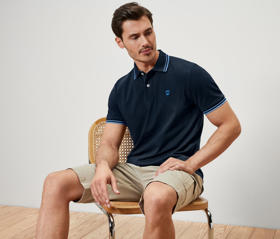 Mann sitzt auf einem Stuhl und trägt ein dunkelblaues Piqué-Poloshirt.