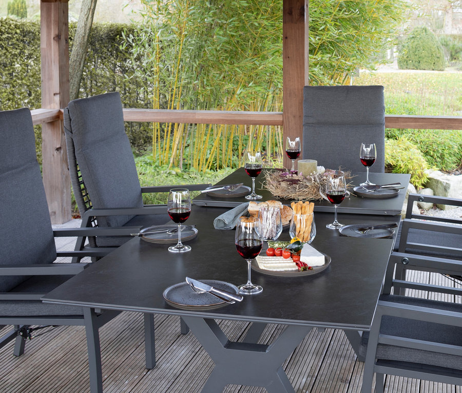 Ein graues deVries Dining-Set mit sechs Stühlen steht auf einer Terrasse mit einem gedeckten Tisch.
