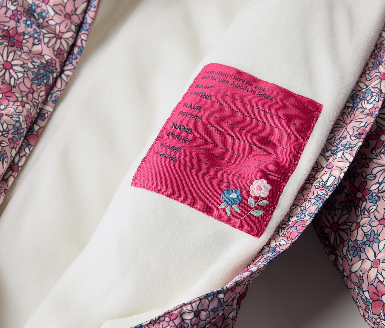 Detailansicht eines Baby-Winteroveralls mit Blumenmuster und Namensschild.