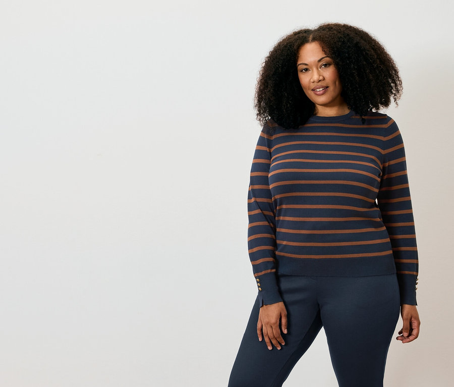 Eine Frau posiert in einem gestreiften Pullover und einer Hose.