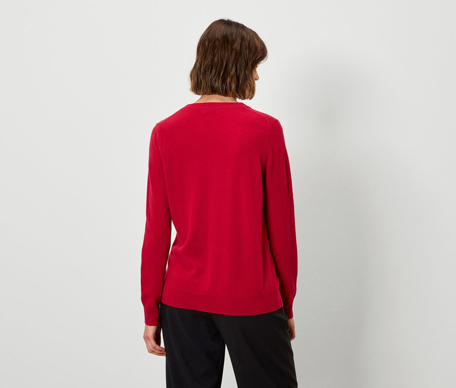 Von hinten ist eine Frau mit kurzen braunen Haaren in einem roten Pullover und einer schwarzen Hose zu sehen.