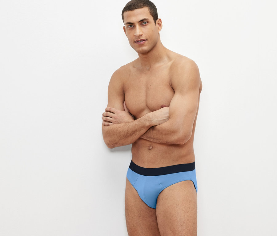 Mann posiert mit verschränkten Armen und trägt blaue 4 Slips.