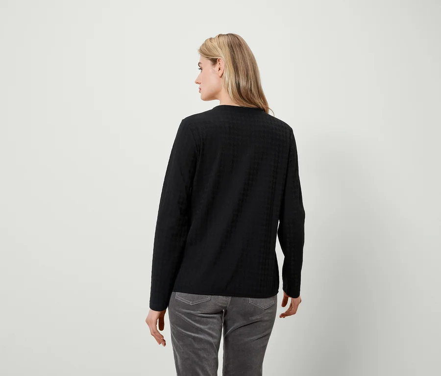 Frau schaut über die Schulter nach links, trägt ein schwarzes Langarmshirt und graue Hosen.