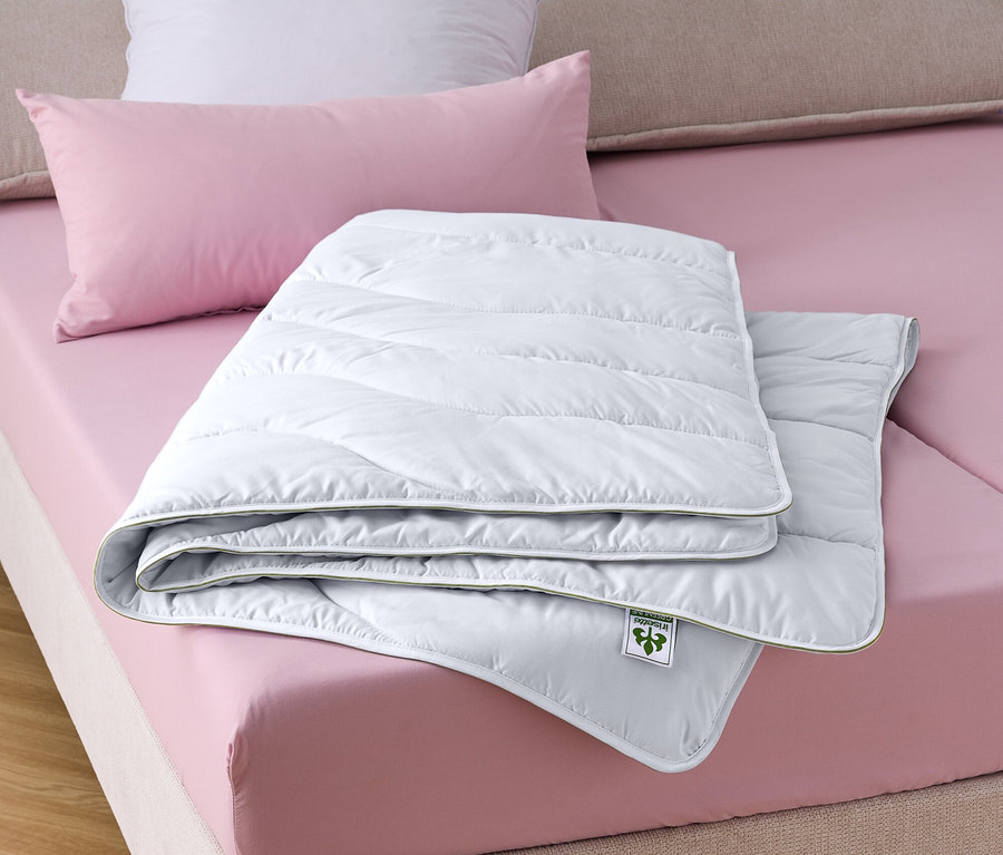 Auf einem Bett liegt eine irisette® greenline Steppdecke Dacron®-Aktivkohle.