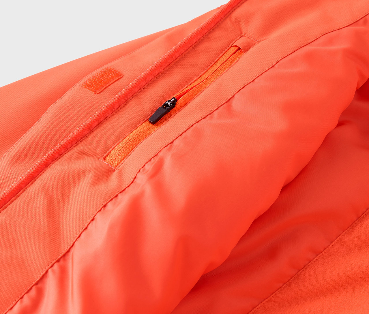 Detail einer orangefarbenen Jacke mit Reißverschluss und Tasche.