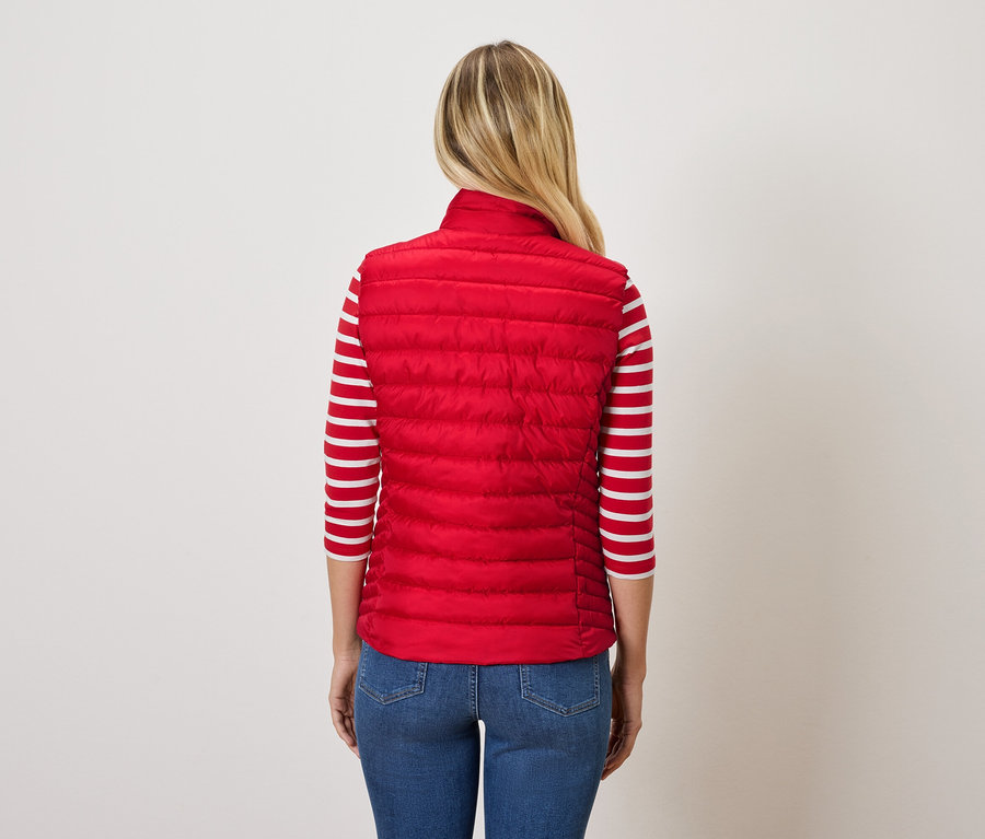 Rückansicht einer blonden Frau, die eine rote Steppweste und blaue Jeans trägt.