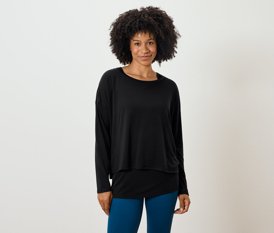 Frau mit Afro-Frisur posiert in einem schwarzen, langärmligen Oberteil und blauen Leggings.