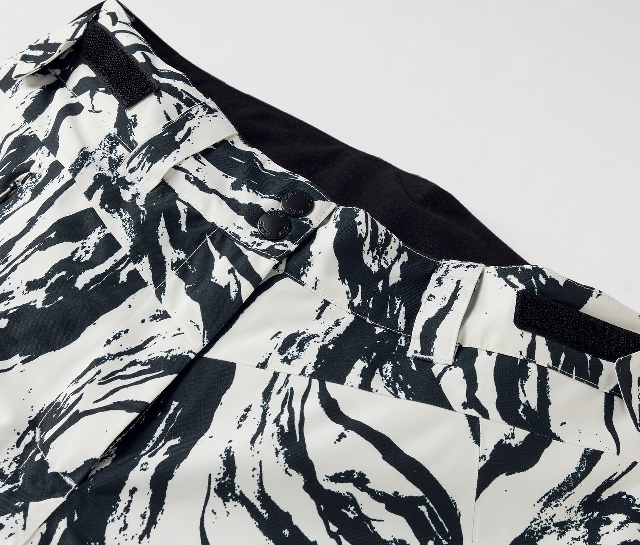 Detail einer Hose mit schwarz-weißem Muster, Knopfverschluss und schwarzem Bund.