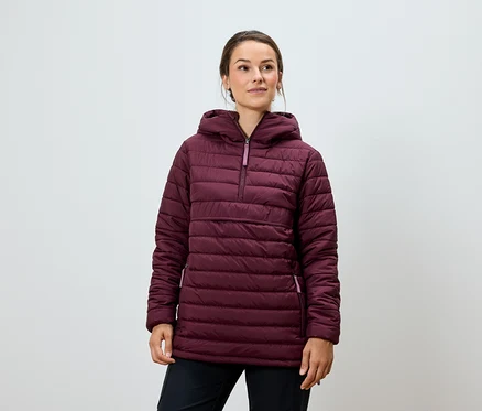 Eine Frau posiert in einer burgunderfarbenen Steppjacke mit Kapuze und einer schwarzen Hose.