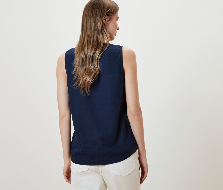 Frau trägt eine ärmellose Leinenbluse, navy, und weiße Hosen.