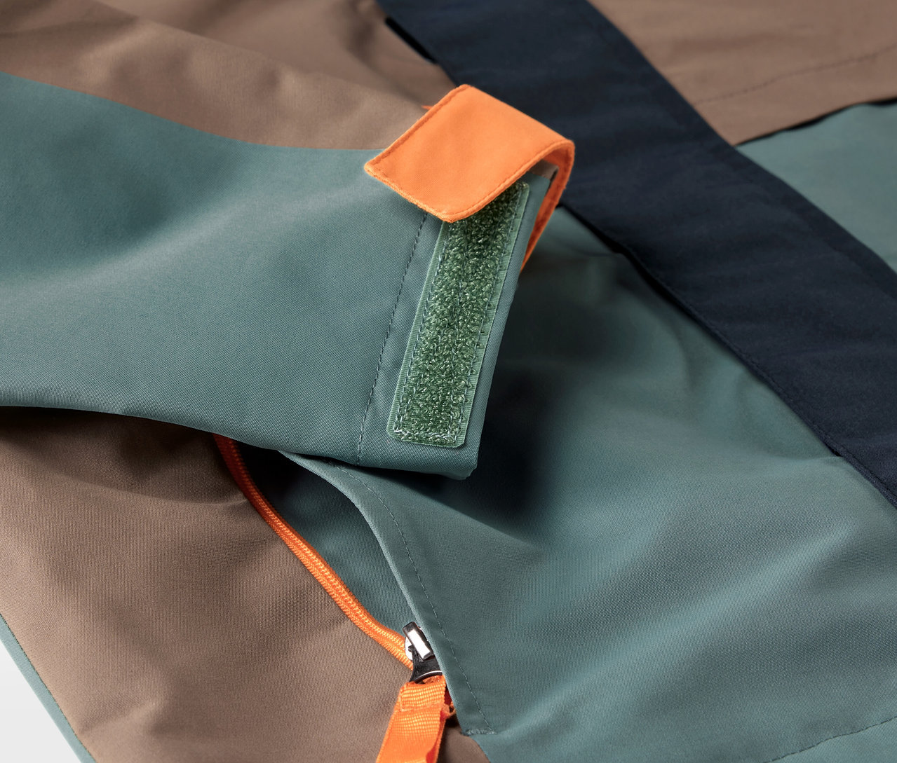 Detailansicht einer Kinder-Allwetterjacke mit Reißverschlusstasche und Klettverschluss am Ärmel.