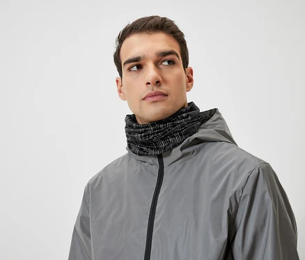 Mann mit braunen Haaren trägt eine graue Kapuzenjacke und einen schwarzen Halswärmer.