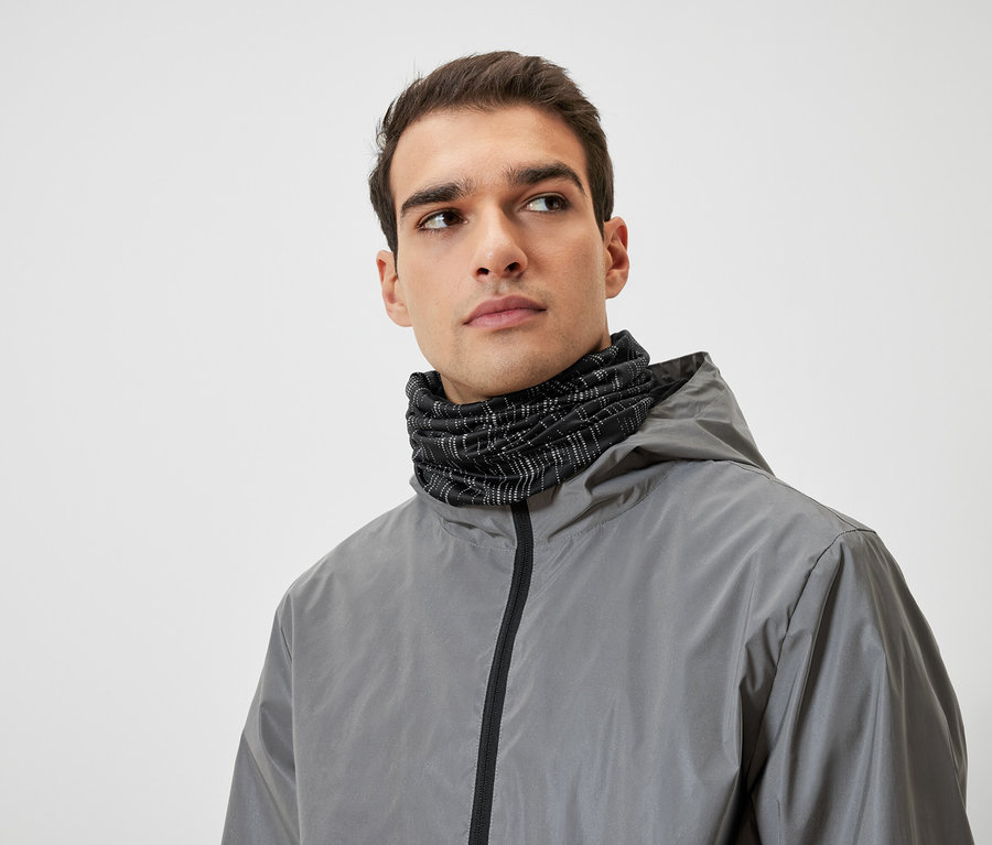 Mann mit braunen Haaren trägt eine graue Kapuzenjacke und einen schwarzen Halswärmer.