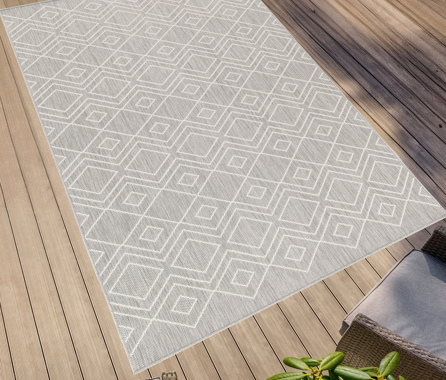 Grauer, faltbarer Outdoor-Teppich »Diamond Rhythm« mit weißem geometrischen Muster auf Holzdeck.