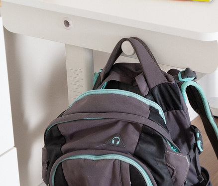 Ein grauer Rucksack mit türkisfarbenen Akzenten hängt an einem weißen Schreibtisch.