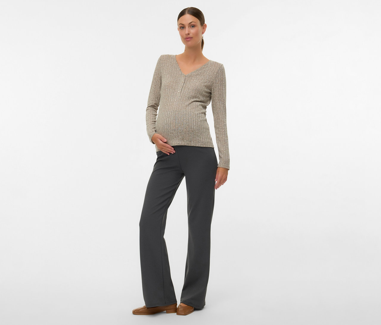 Frau mit Dutt trägt MAMALICIOUS Shirt »MLPAMMIE LIA«, graue Hose und braune Schuhe, Hand auf Bauch.