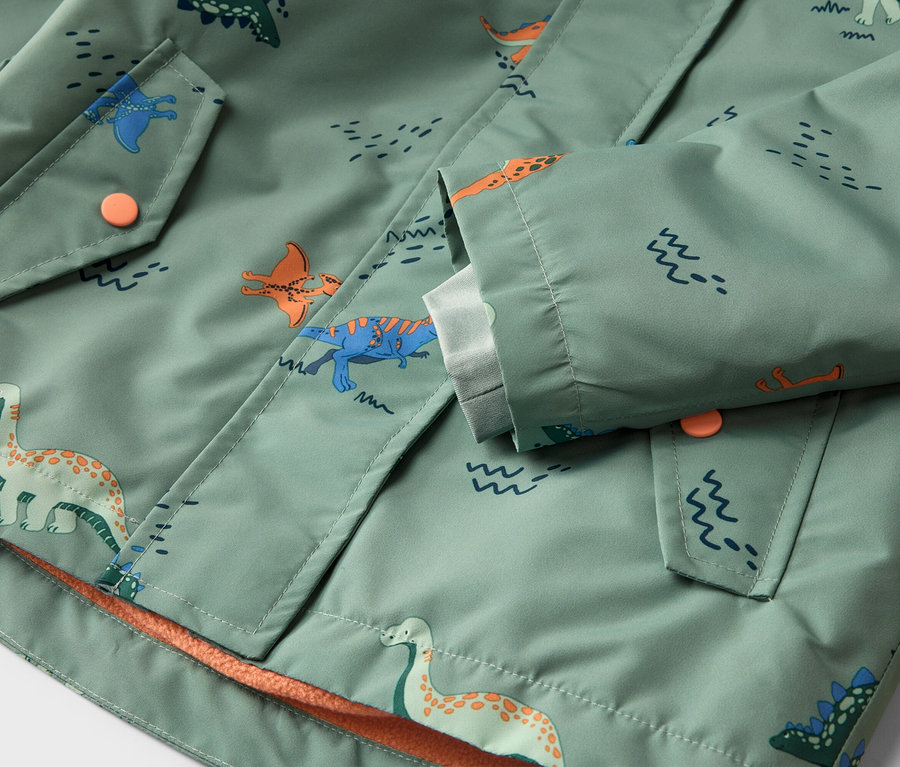 Nahaufnahme einer hellgrünen Jacke mit Dinosaurier-Muster, Knopfverschluss und Taschen.