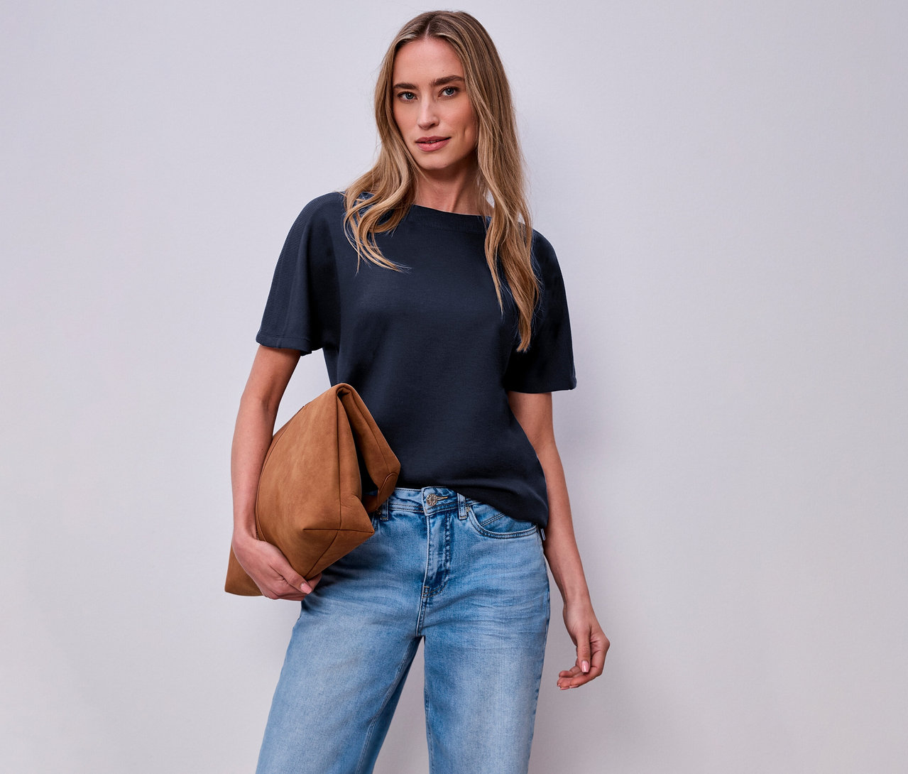 Frau mit brauner Tasche und Street One Kurzarmshirt in Navy vor einer weißen Wand.