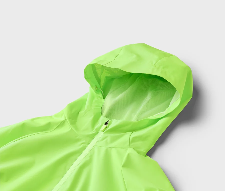 Nahaufnahme einer hellgrünen Regenjacke mit Kapuze und Reißverschluss vor einem grauen Hintergrund.