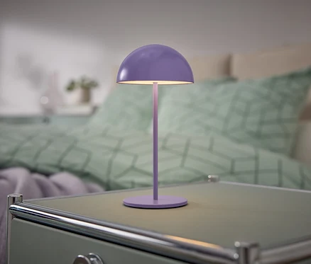 Eine lila Lampe steht auf einem Nachttisch neben einem Bett.