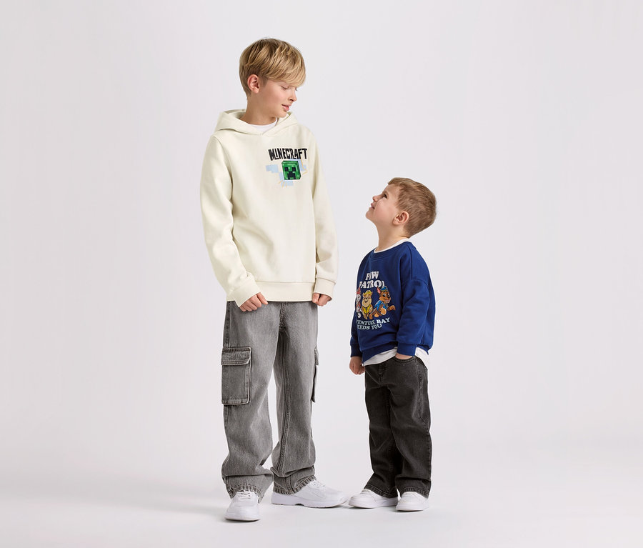 Zwei Jungen stehen vor einem weißen Hintergrund. Der größere Junge trägt einen MINECRAFT Kinder-Hoodie mit angerauter Innenseite.