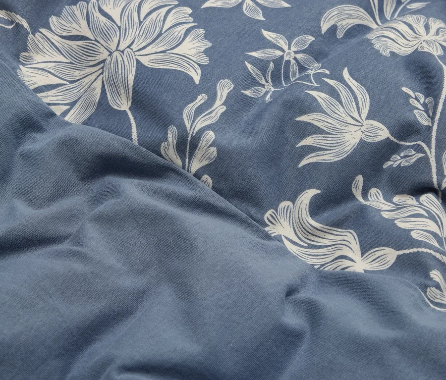 Blauer Stoff mit weißem Blumenmuster auf der rechten Seite, gefaltet, um einen einfarbigen blauen Bereich auf der linken Seite zu zeigen.