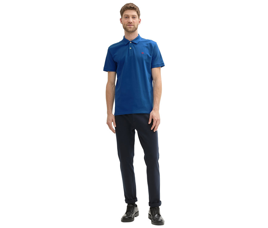 Mann in marineblauer Hose und blauem Tom Tailor Piqué Poloshirt, Advanced Blue, mit rotem Logo, posiert vor einem weißen Hintergrund.