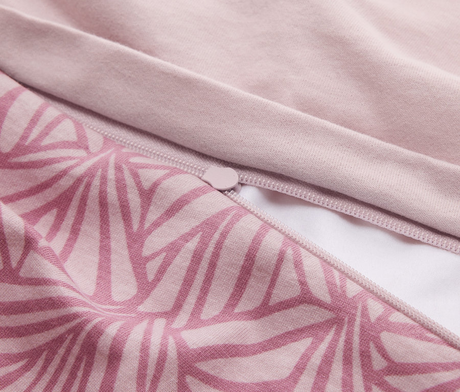 Nahaufnahme eines Stoffes in zwei Rosatönen. Ein Teil zeigt ein geometrisches Muster in dunklerem Rosa, der andere Teil ist einfarbig hellrosa. Ein rosa Reißverschluss ist teilweise geöffnet und gibt den Blick auf ein weißes Futter frei.
