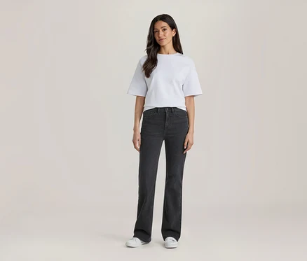 Frau steht in einem weißen T-Shirt, dunkelgrauen Jeans und weißen Turnschuhen.