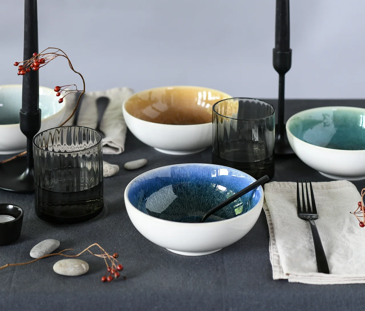 Ein gedeckter Tisch mit vier Schalen des creaTable Bowl-Sets »Caldera« in Blau, Gelb und Türkis, dazu Gläser, Besteck und Kerzen.