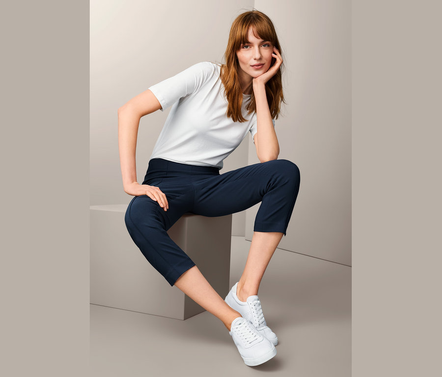 Frau sitzt und trägt eine blaue 7/8-Stretchhose und ein weißes T-Shirt.