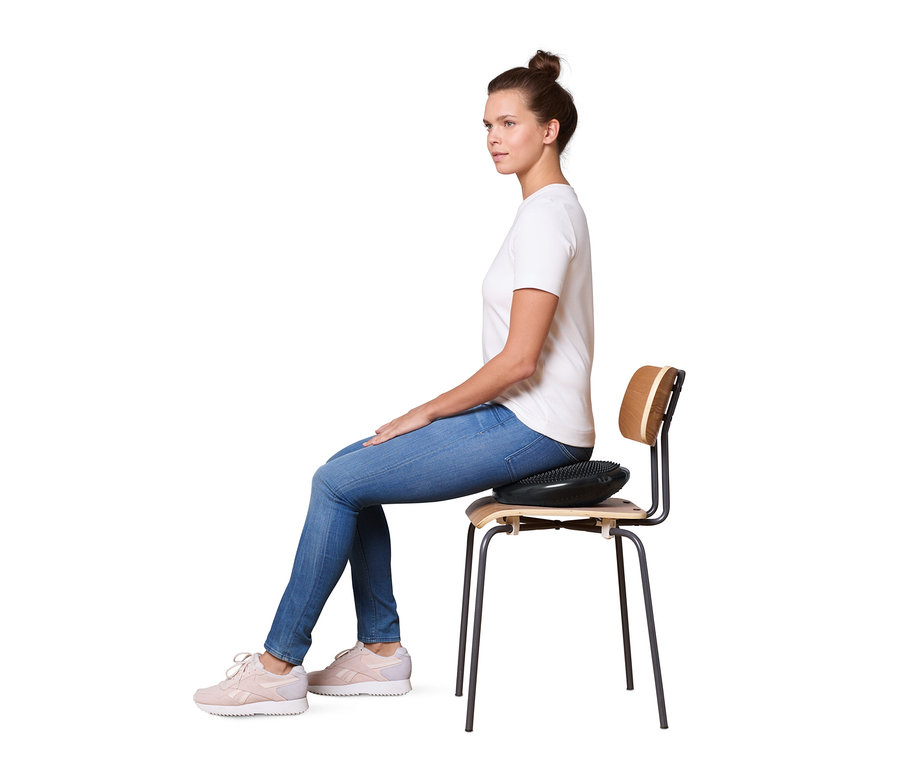 Frau sitzt mit einem Balance-Kissen auf einem Stuhl.