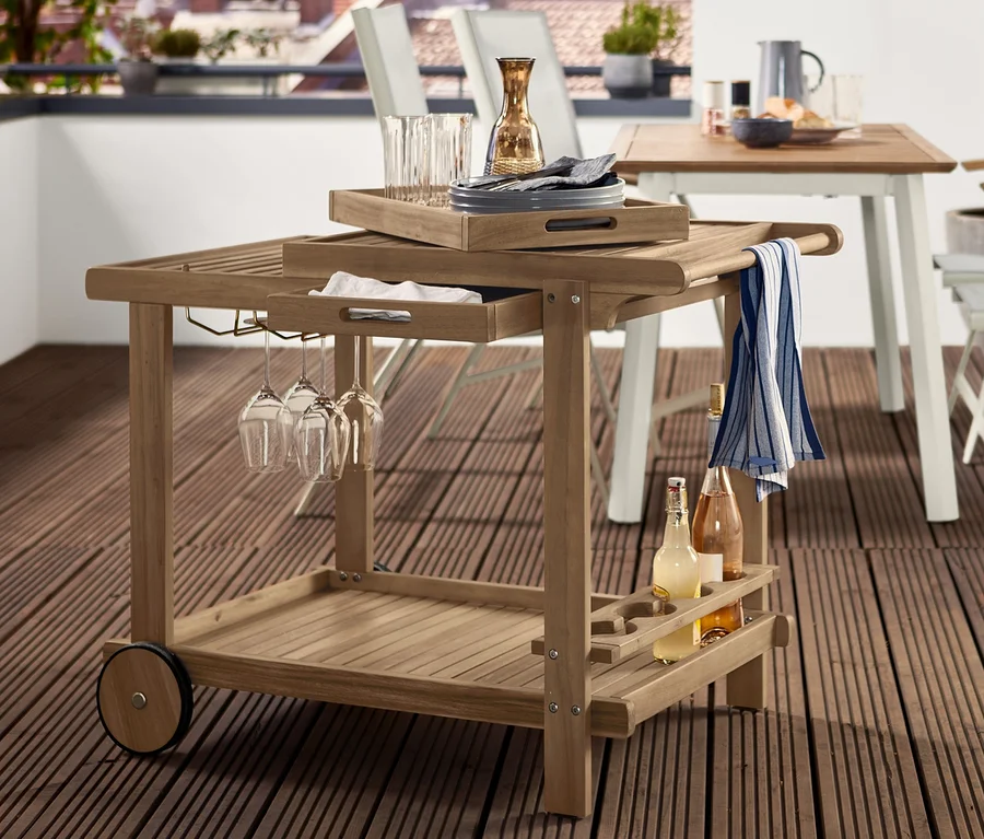 Auf einer Terrasse stehen ein Grillwagen »Lenja« mit 2 Tabletts, eine Solarlaterne aus Holz, ein Esstisch und Stühle.