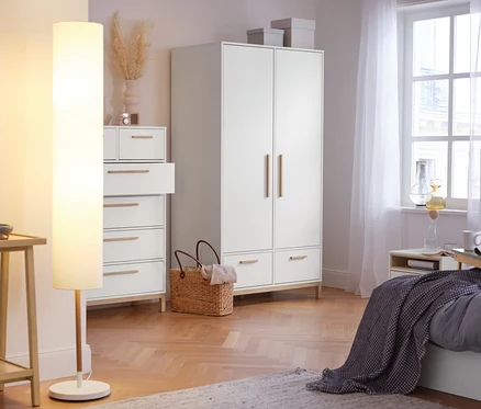 Im Schlafzimmer stehen ein Konsolentisch mit 2 Ablagen, eine Stehleuchte mit Textilschirm, ein Highboard »Eklund« mit Schubladen und ein Kleiderschrank »Eklund« mit Schubladen.