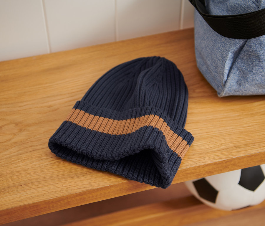 Eine Strickmütze und eine Sporttasche liegen auf einem Holzregal.