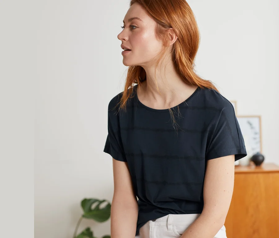 Frau sitzt und trägt ein dunkelblaues Shirt mit Rundhalsausschnitt.