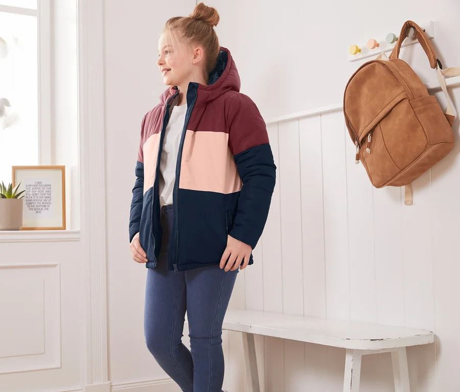 Mädchen in Thermojacke im Colorblocking-Design steht im Zimmer.