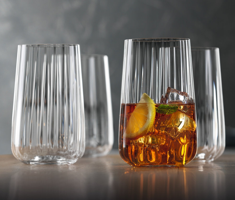 Vier Spiegelau Longdrinkgläser »Lifestyle« stehen auf einem Tisch, eines davon ist mit einem Getränk, Eis und einer Zitronenscheibe gefüllt.