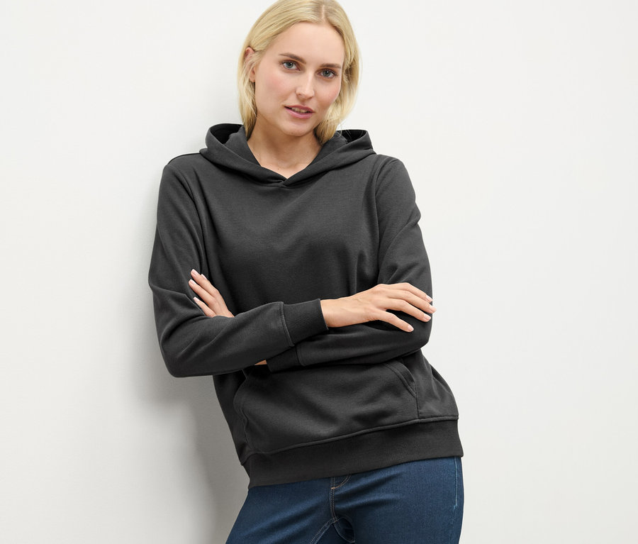 Blonde Frau posiert in anthrazitfarbenem Hoodie.
