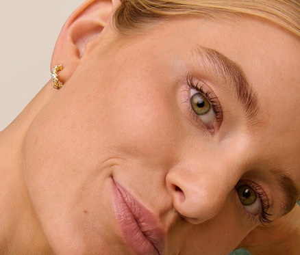 Blonde Frau lehnt auf einem grünen Sofa und trägt 925 Silber Creolen Wave.