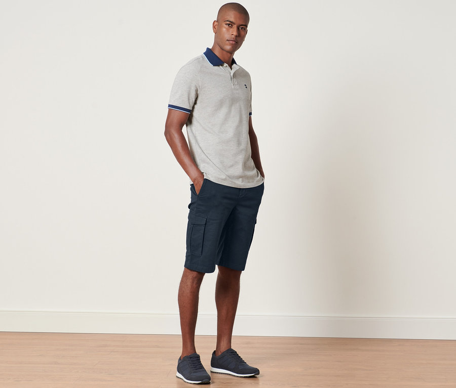 Mann steht mit Händen in den Taschen der navy Cargo-Shorts.