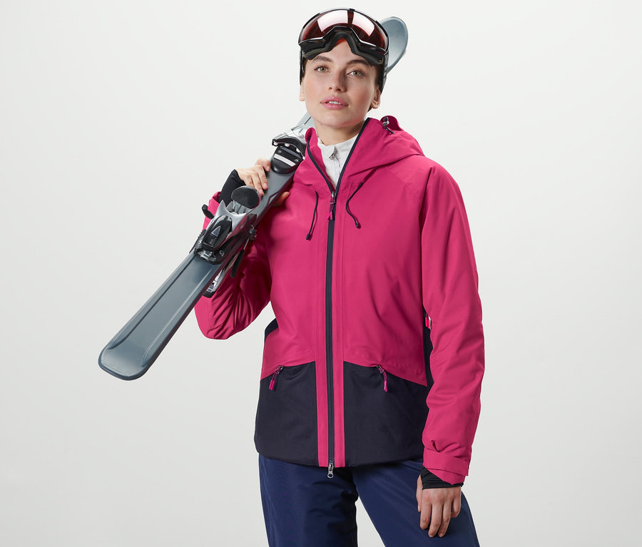 Frau hält Ski über der Schulter. Sie trägt eine Skijacke.