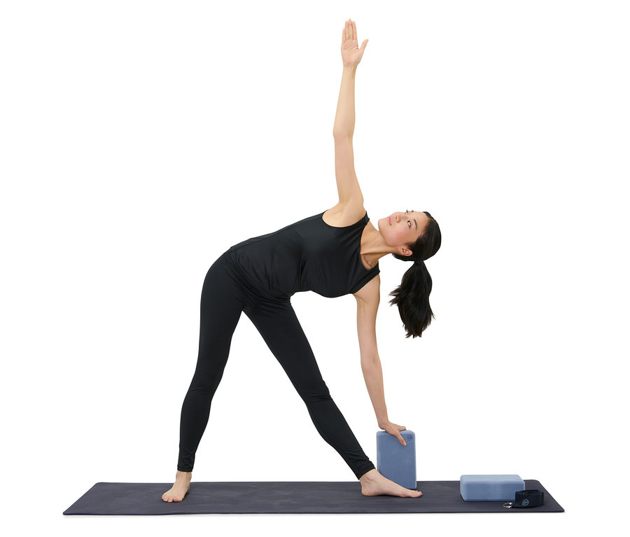 Frau in schwarzer Sportbekleidung macht Dreieckspose mit Yoga-Set.
