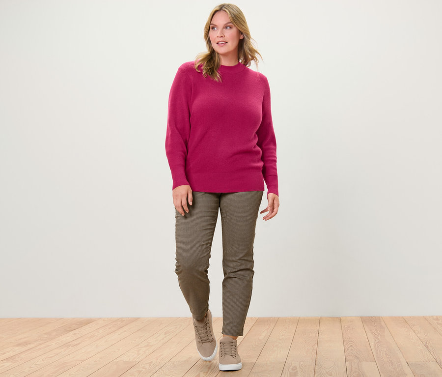 Frau geht, trägt himbeerroten Feinstrickpullover und Stretchhose mit Hahnentritt-Jacquard.