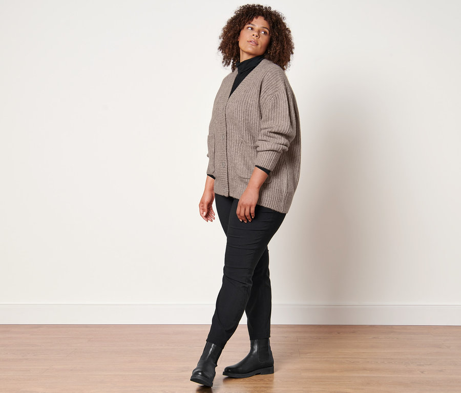 Frau posiert in Grobstrick-Cardigan mit Wolle, schwarzem Rollkragenshirt, schwarzer Konfektionierter Bengalinhose und Lederboots.